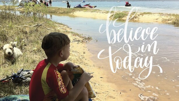 Une scène de plage avec une tente, des personnes et un bateau. On peut voir le texte suivant : « Croyez au présent ».