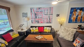 Un salon avec un canapé en cuir noir, une table basse en bois et une œuvre d’art murale représentant des noms de villes.