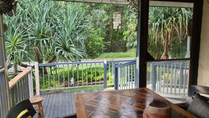 Une table et des chaises en bois sur un balcon donnant sur un jardin et des arbres.