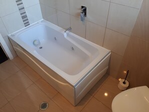 Een bad/douchecombinatie, een bubbelbad, een haardroger, handdoeken