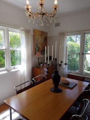 A dining room with a wooden table, chairs, a chandelier, and a painting on the wall. - Moonya, the writer's retreat, the 1950s vintage  holiday home and house gallery (Katoomba)