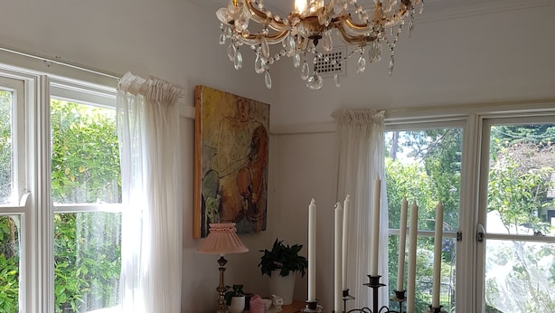 A dining area with a wooden table, chairs, a chandelier, a painting, and windows with curtains.