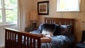 A bedroom with a wooden bed, a nightstand, a lamp, a framed picture on the wall, and a window with curtains.