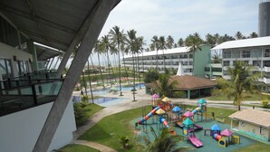 Ein Hotelinnenhof mit Kinderspielplatz, Palmen und einem Pool.