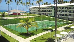 Ein Hotel mit Tennisplatz, Palmen und Blick auf den Strand.