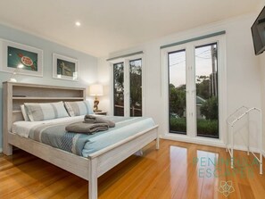 A bedroom with a bed, a nightstand, a lamp, and a window with a view of greenery.