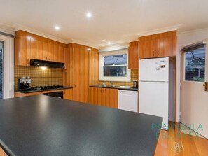 A modern kitchen with wooden cabinets, a black countertop, a built-in stove, and a white refrigerator.