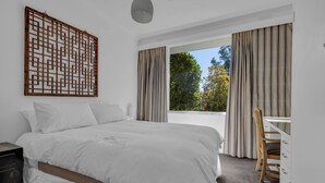 A bedroom with a large bed, a desk, and a view of trees through the window.
