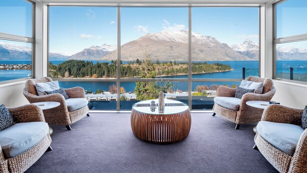 A spacious room with large windows offering a view of a lake and mountains. There are wicker sofas and a round coffee table. - Panorama, Queenstown (Queenstown Hill)
