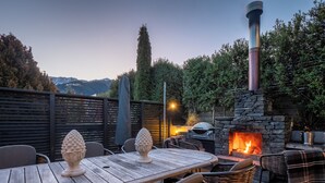 An outdoor patio with a stone fireplace, wicker chairs, and a wooden table. - Panorama, Queenstown (Queenstown Hill)