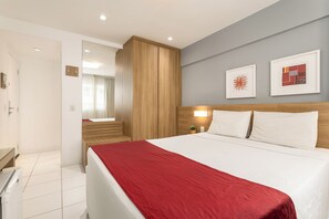 A hotel room with a bed, a nightstand, a mirror, a wooden wardrobe, and two framed artworks on the wall.