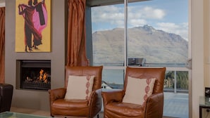 A room with two leather armchairs, a fireplace, and a large window with a mountain view. - Lake View Villa | Great location | Amazing views (Queenstown)