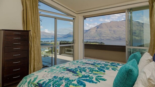 A bedroom with a large bed, a dresser, and a balcony with a mountain view. - Lake View Villa | Great location | Amazing views (Queenstown)