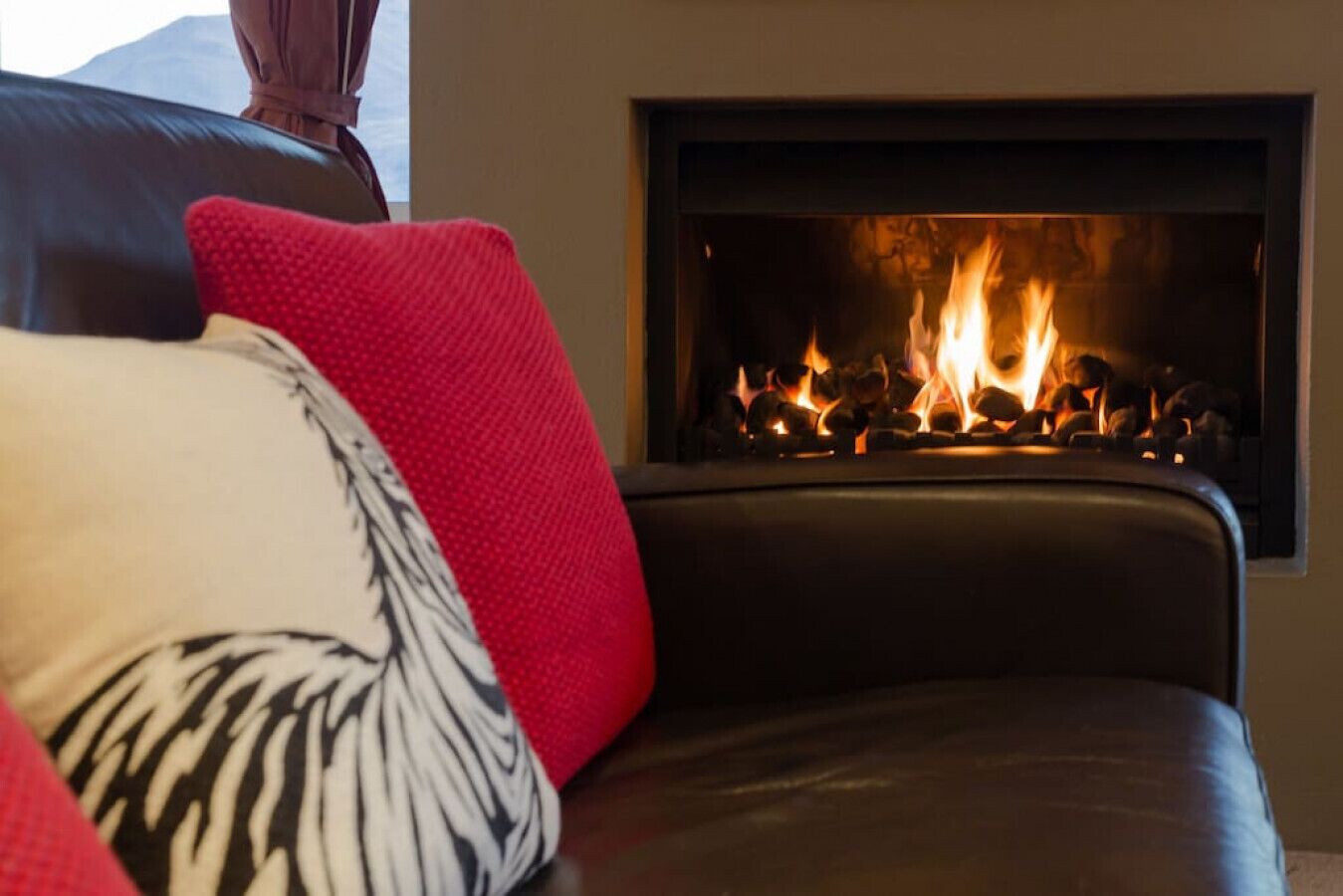 A living room with a fireplace, a leather sofa, and a red and white pillow.