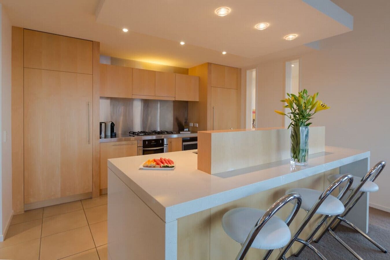 Una cocina moderna con armarios de madera, una isla central con taburetes y un florero con flores.