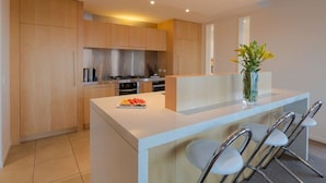 A modern kitchen with wooden cabinets, a central island with bar stools, and a vase with flowers. - Lake View Villa | Great location | Amazing views (Queenstown)