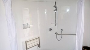 Un área de ducha pequeña y cerrada con un cabezal de ducha manual, un perchero y un panel de control.