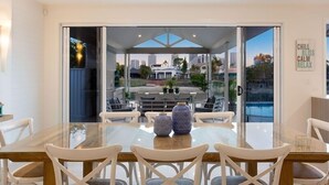 Un comedor moderno con una mesa de vidrio y sillas blancas, vista a la ciudad a través de grandes puertas de vidrio, y un letrero en la pared que dice 'CHILL BLISS CALM RELAX'.