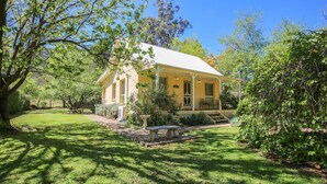 Une maison jaune avec un porche, entourée d’une végétation luxuriante et d’arbres.