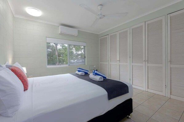 A hotel room with a bed, a ceiling fan, a window, and a set of closets.