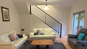 En stue med trappe, en hvid sofa, en lædersofa i brunt skind og et træbord.