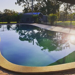 Piscina nítida amb una zona pavimentada al voltant, envoltada per una tanca i arbres.