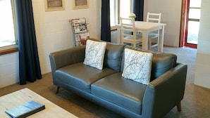 Uma sala de estar com sofá de couro cinza, mesa de centro de madeira, mesa de jantar com cadeiras e ar-condicionado fixado na parede.
