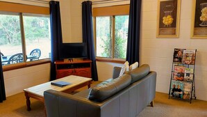 Uma sala de estar com sofá, mesa de centro, televisão em um suporte, armário pequeno e porta-revistas.