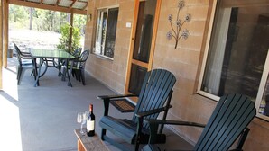 Um pátio externo com mesa, cadeiras, um banco e uma garrafa de vinho.