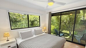 A bedroom with a large bed, a ceiling fan, a window with a view of greenery, and a sliding glass door leading to an outdoor area. - ALL NEW Tessies House-150m to river-7 min. walk to town-pets welcome-quiet court (Bright)