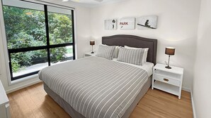 A bedroom with a large window, a bed with striped bedding, two bedside tables with lamps, a ceiling fan, and artwork on the wall. - ALL NEW Tessies House-150m to river-7 min. walk to town-pets welcome-quiet court (Bright)