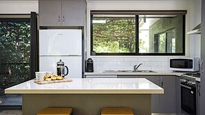 A modern kitchen with a central island, two stools, a refrigerator, a microwave, and a window with a view of greenery. - ALL NEW Tessies House-150m to river-7 min. walk to town-pets welcome-quiet court (Bright)