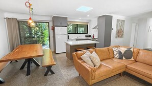 A modern living room with a wooden dining table, a brown leather sofa, and a kitchen in the background. - ALL NEW Tessies House-150m to river-7 min. walk to town-pets welcome-quiet court (Bright)