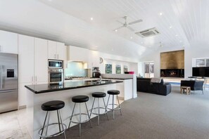 A modern kitchen with a central island, bar stools, and a dining area with a sofa and TV.