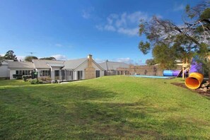 A residential property with a grassy yard, a house with a chimney, and a playground with a slide.