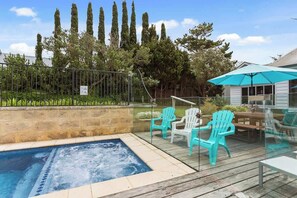 A swimming pool with a hot tub, surrounded by a wooden deck and turquoise Adirondack chairs.