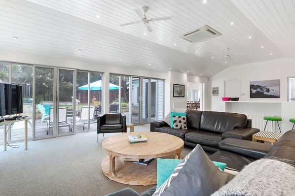 A spacious living room with a large window, a ceiling fan, and a flat-screen TV.