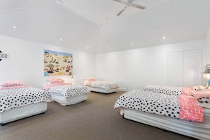 A hotel room with three beds, each with polka dot bedding, a ceiling fan, and a wall art depicting a beach scene.