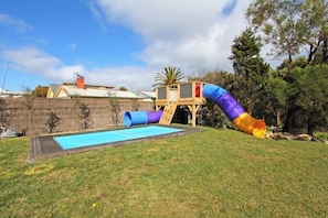 A backyard with a slide, a small pool, and a wooden play structure.