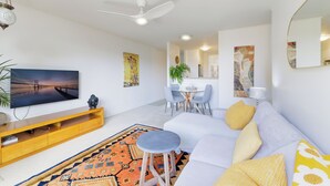 A modern living room with a flat-screen TV, wooden entertainment unit, and a sofa with yellow pillows. - Coastal Calm at Bronte Beachside Escape (Bronte)