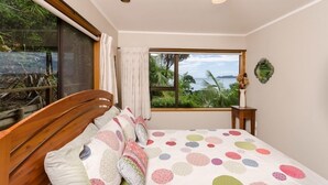 Une chambre à coucher avec un lit, une fenêtre donnant sur un paysage verdoyant et une étendue d’eau, et une petite table sur laquelle est posé un vase.