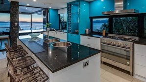 Una cocina moderna con una isla grande, electrodomésticos de acero inoxidable y vistas al mar.