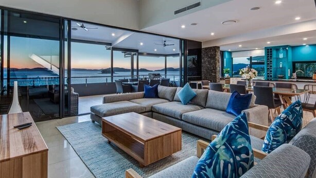 Un amplio salón con un sofá modular grande, una mesa de centro de madera y vistas al océano.