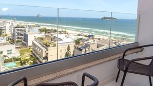 Un balcón con sillas de mimbre que da a una playa y al paisaje urbano.