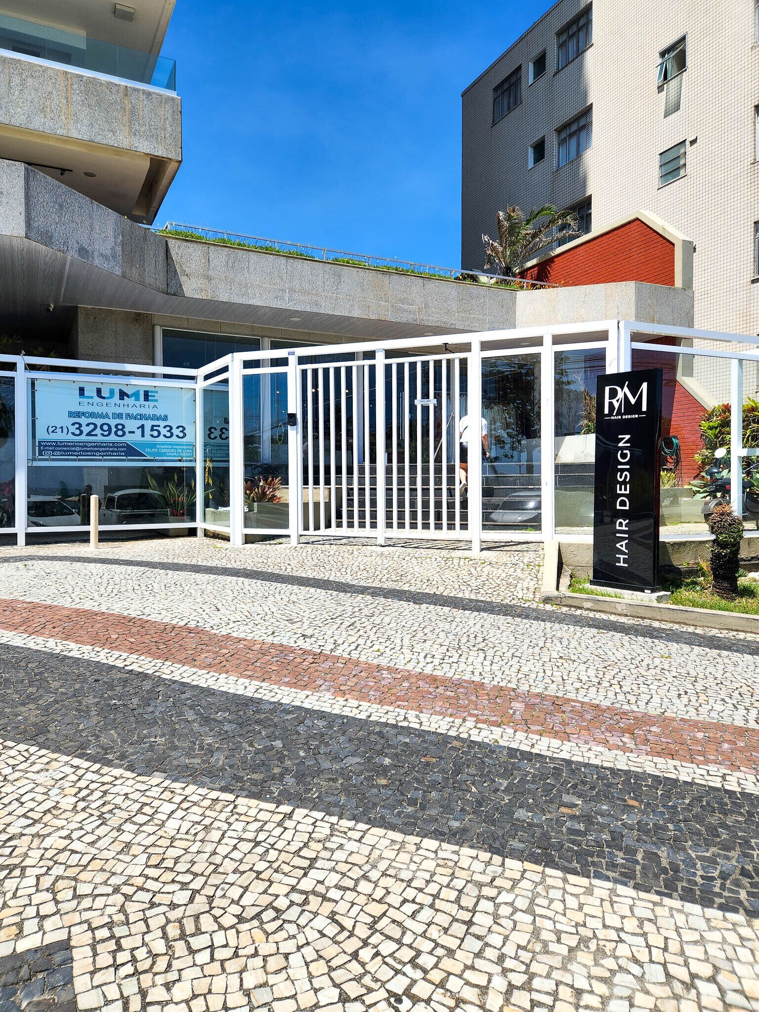 Un edificio moderno con entrada de vidrio, un letrero que dice 'LUME Engenharia' y un letrero que dice 'RM Hair Design'.
