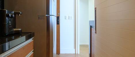 A narrow hallway with wooden flooring, a stainless steel refrigerator, and a coffee maker on the left.