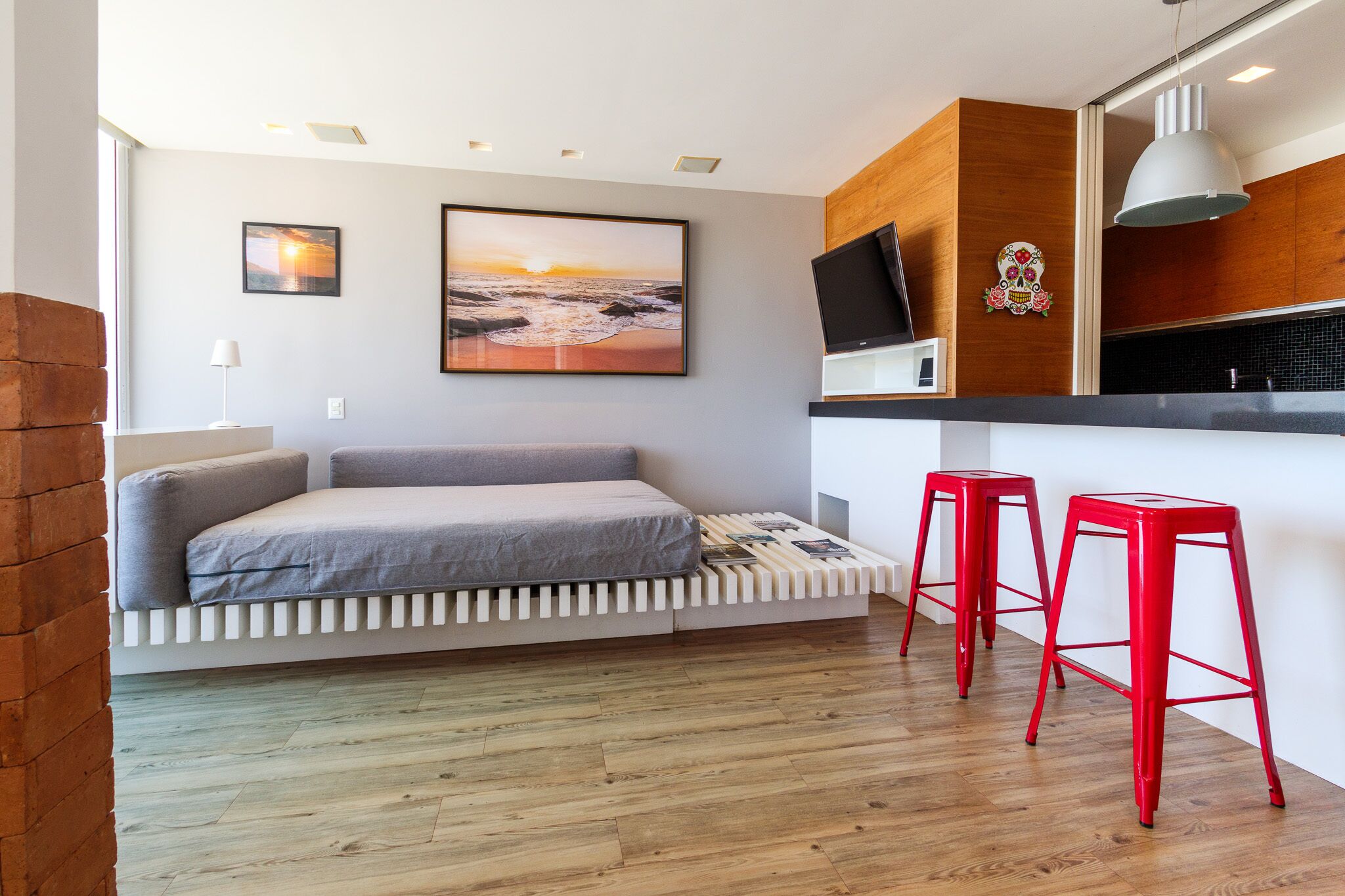 A compact living space with a sofa bed, a TV, and two red stools.