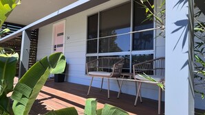 Une véranda avec deux fauteuils en osier, une terrasse en bois et une porte blanche portant le numéro 34.