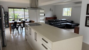Une cuisine moderne dotée d’un grand îlot central, d’un coin repas avec des chaises, d’un canapé en cuir noir et d’une vue sur l’extérieur.