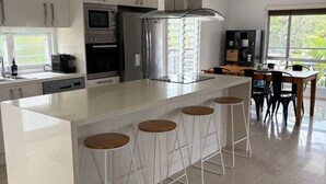 Une cuisine moderne dotée d’un îlot central, de tabourets de bar et d’un coin repas offrant une vue sur la verdure.